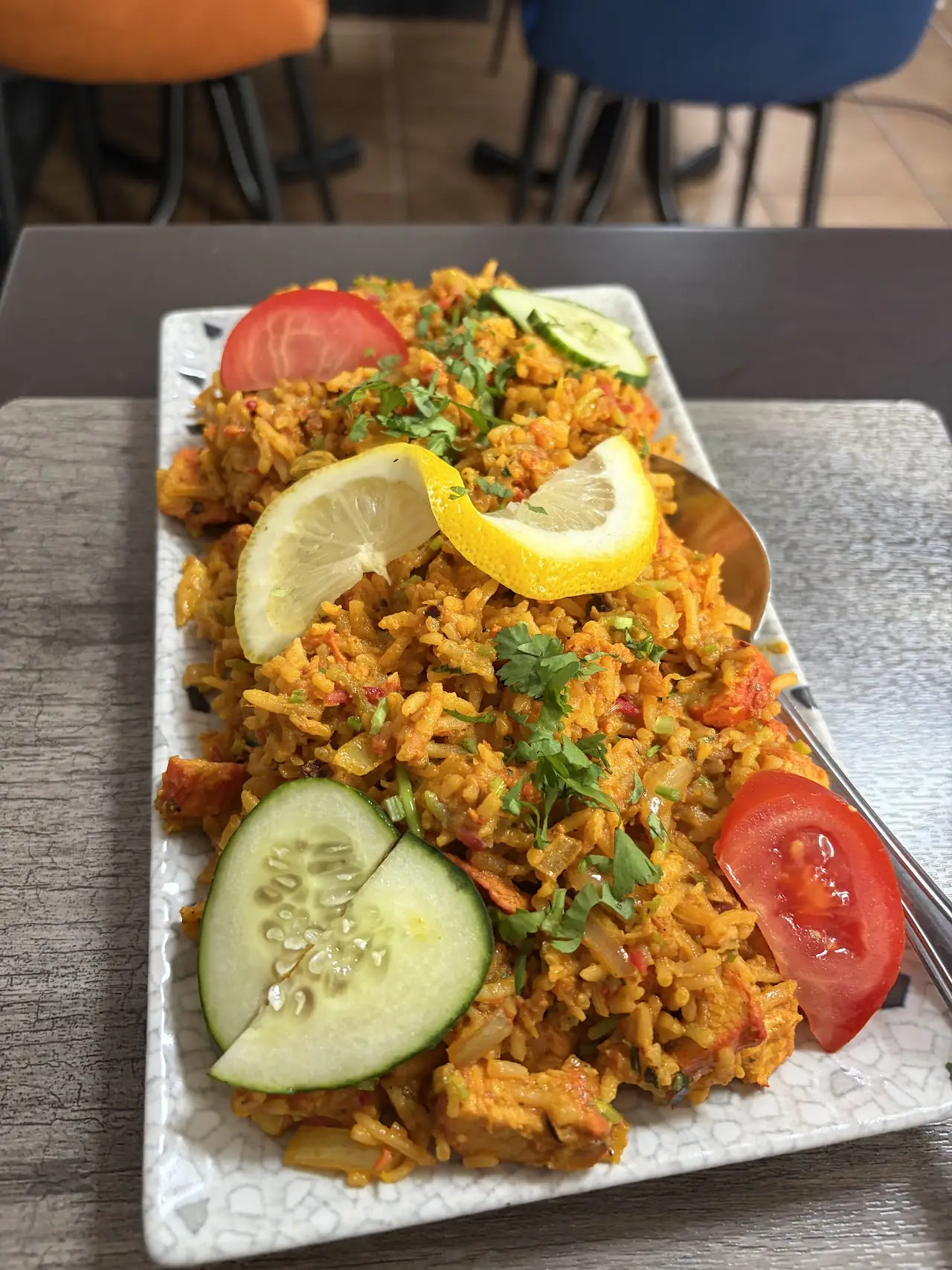 A plate of spiced rice biryani garnished with lemon wedges, cucumber, and tomato.