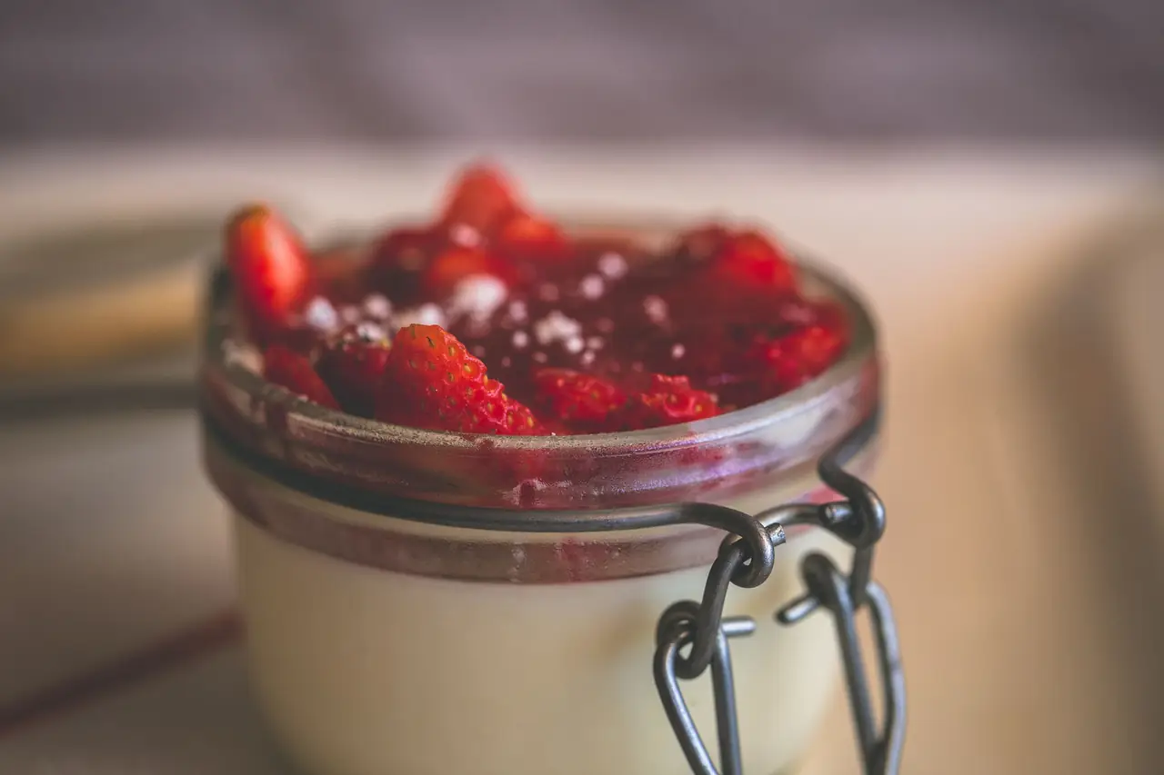 Small glass jar dessert layered with cream and topped with fresh sliced strawberries in syrup, Kata