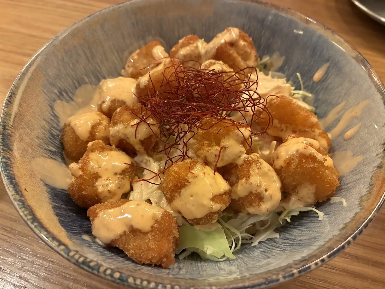 A bowl of crispy fried chicken bites in a creamy sauce with crispy garnish