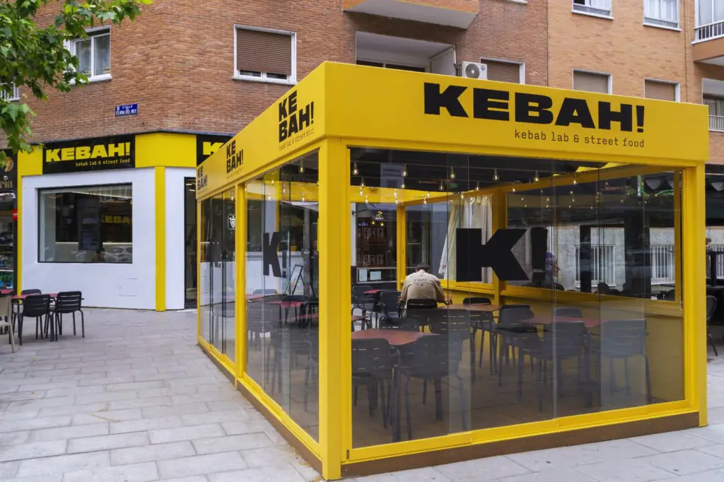 Corner storefront of Kebah kebab lab and street food with a bright yellow glass-walled dining pod and branded signage on a brick building