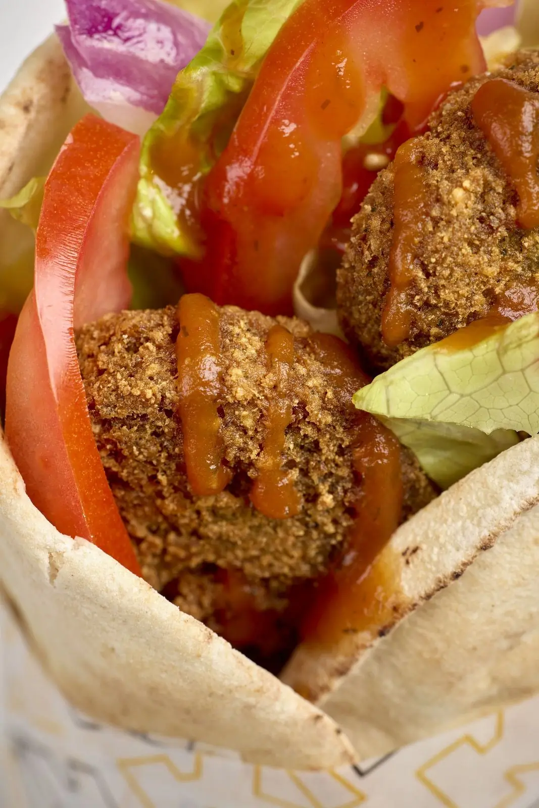 A pita wrap filled with breaded fried filling, lettuce, and tomato.
