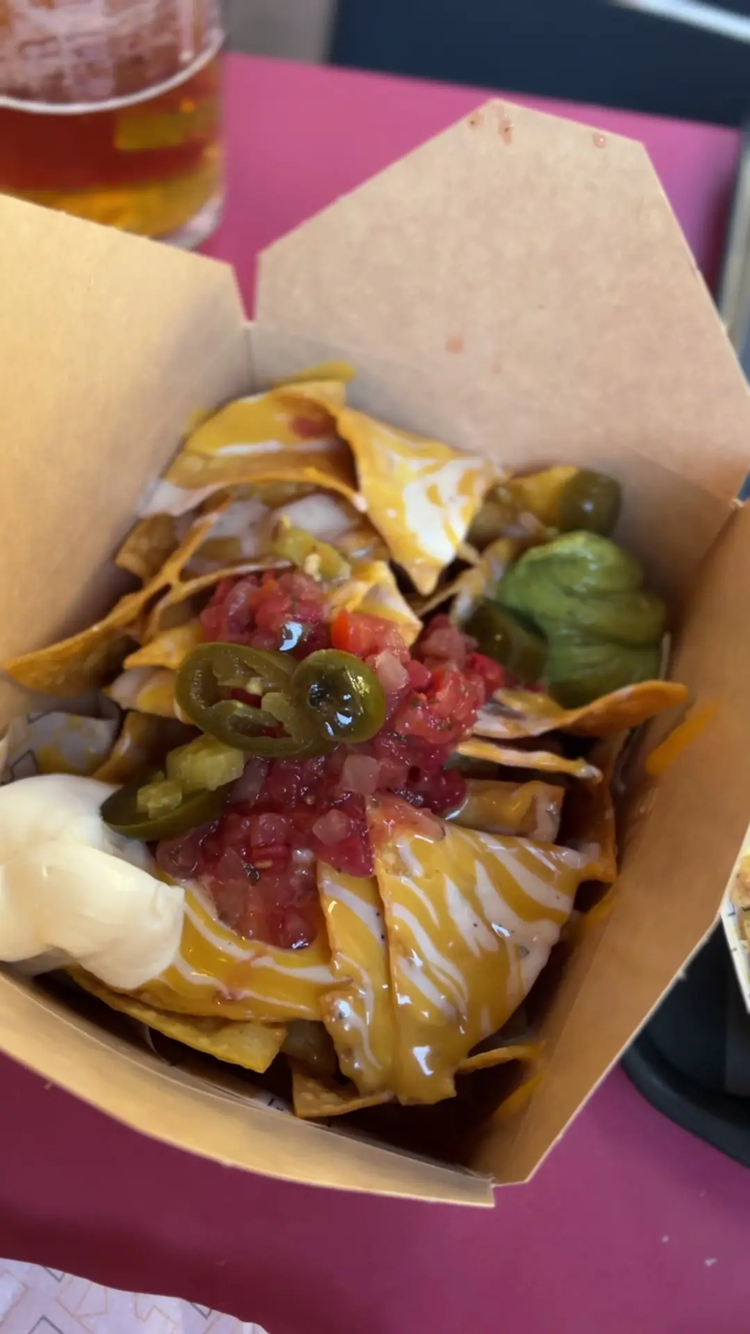 A box of loaded tortilla chips with melted cheese, salsa, and pickled jalapeños.