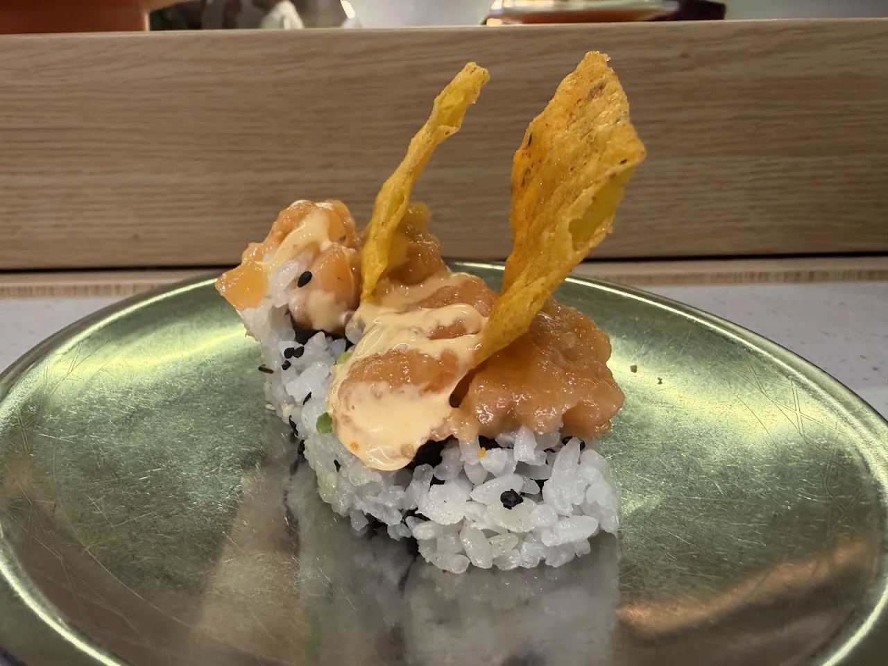 A sushi roll topped with a fried tempura strip and creamy sauce