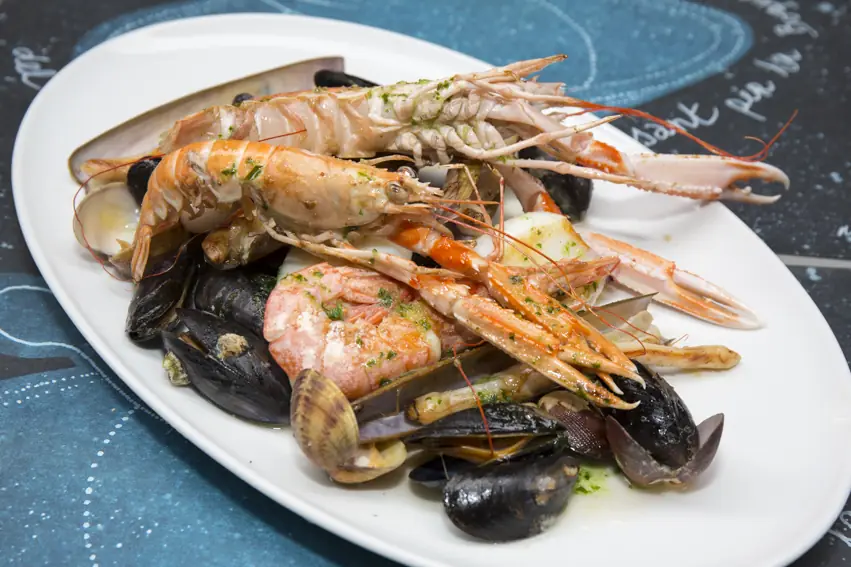 Mixed seafood platter with grilled prawns, langoustines, mussels, and clams on a white oval plate, Kiosk Universal