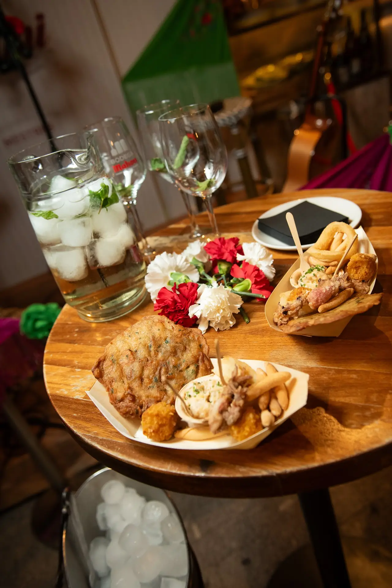 Wooden boats of fried tapas including calamari rings and croquettes beside a jug of sangria on ice