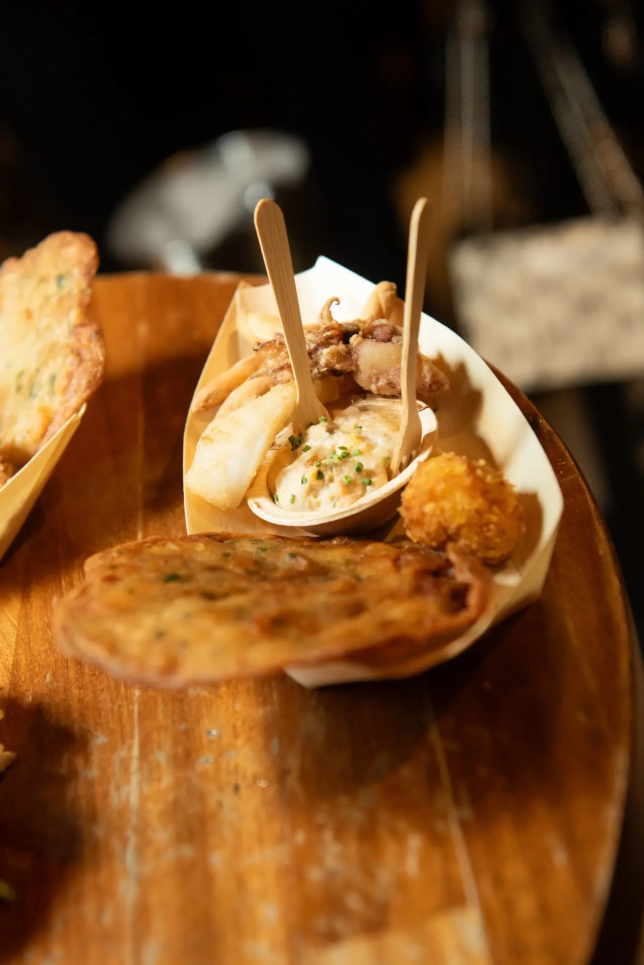 Close-up of a wooden tapas boat with fried calamari, fries, a croquette and a seafood dip