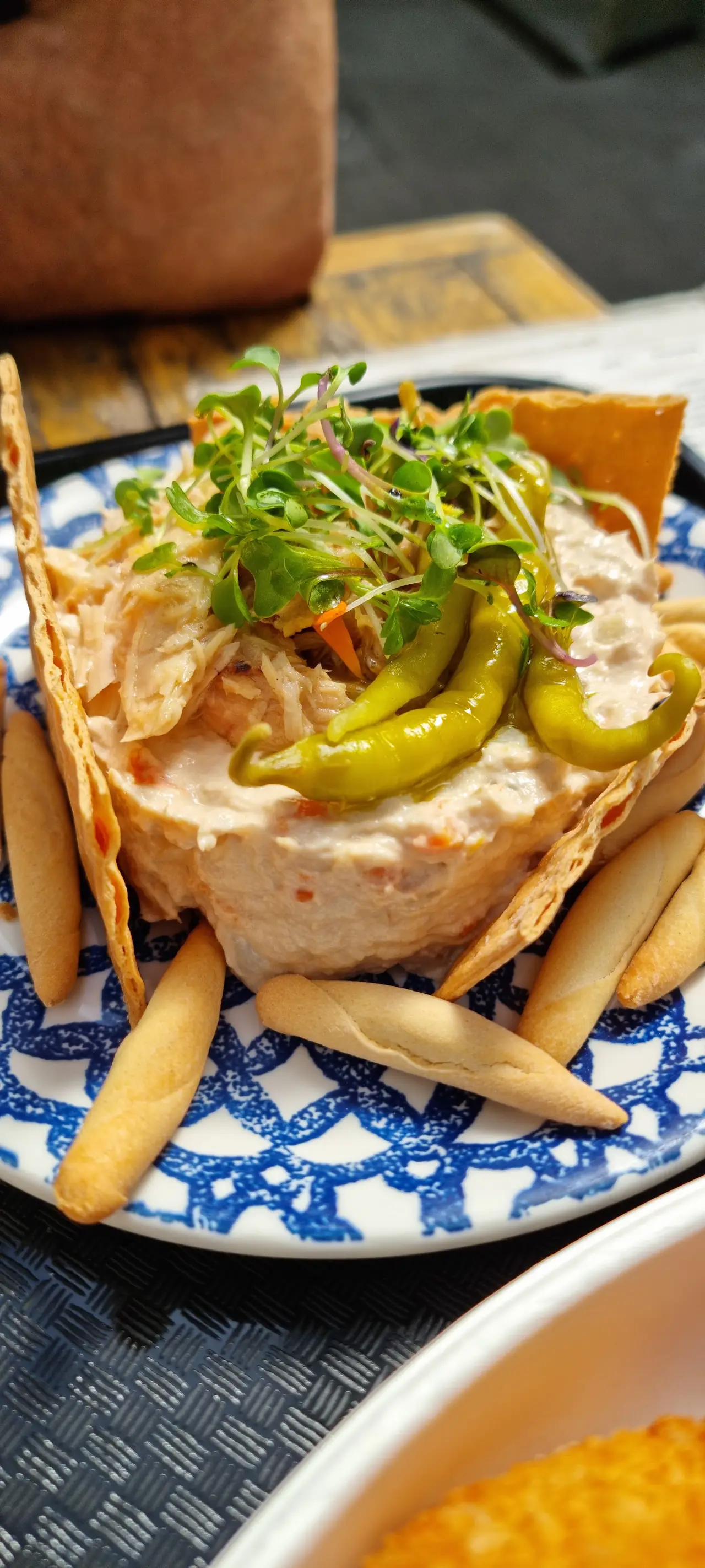 Plated dish of shredded fish salad topped with microgreens and guindilla peppers, with picos and crackers