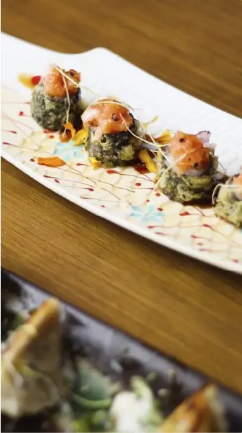 Three fried green croquette bites topped with diced salmon and microgreens on a long white plate with sauce drizzles