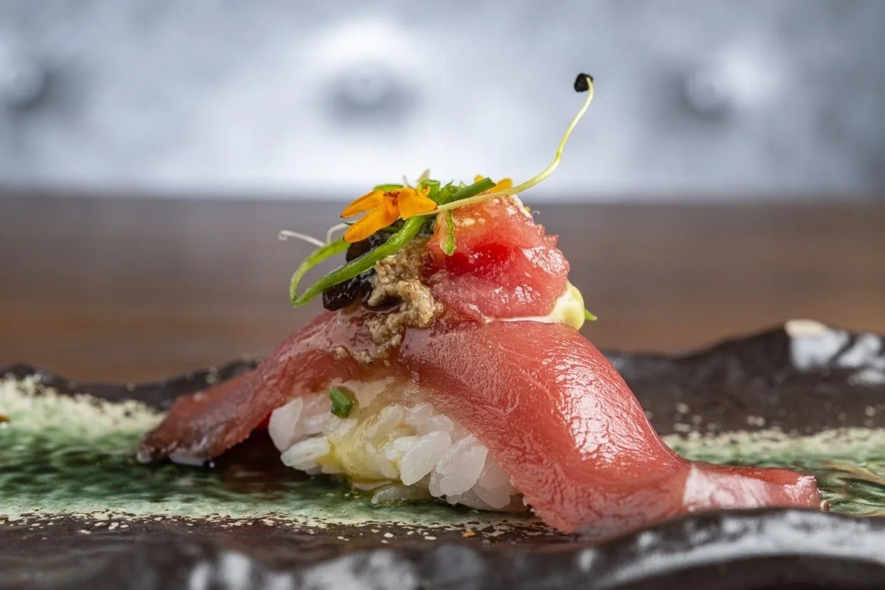A single piece of tuna nigiri with garnish on a leaf-patterned plate