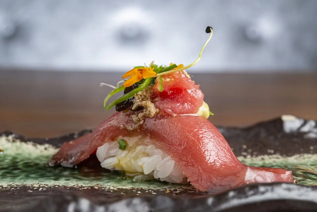 A single piece of tuna nigiri garnished with a small yellow flower.