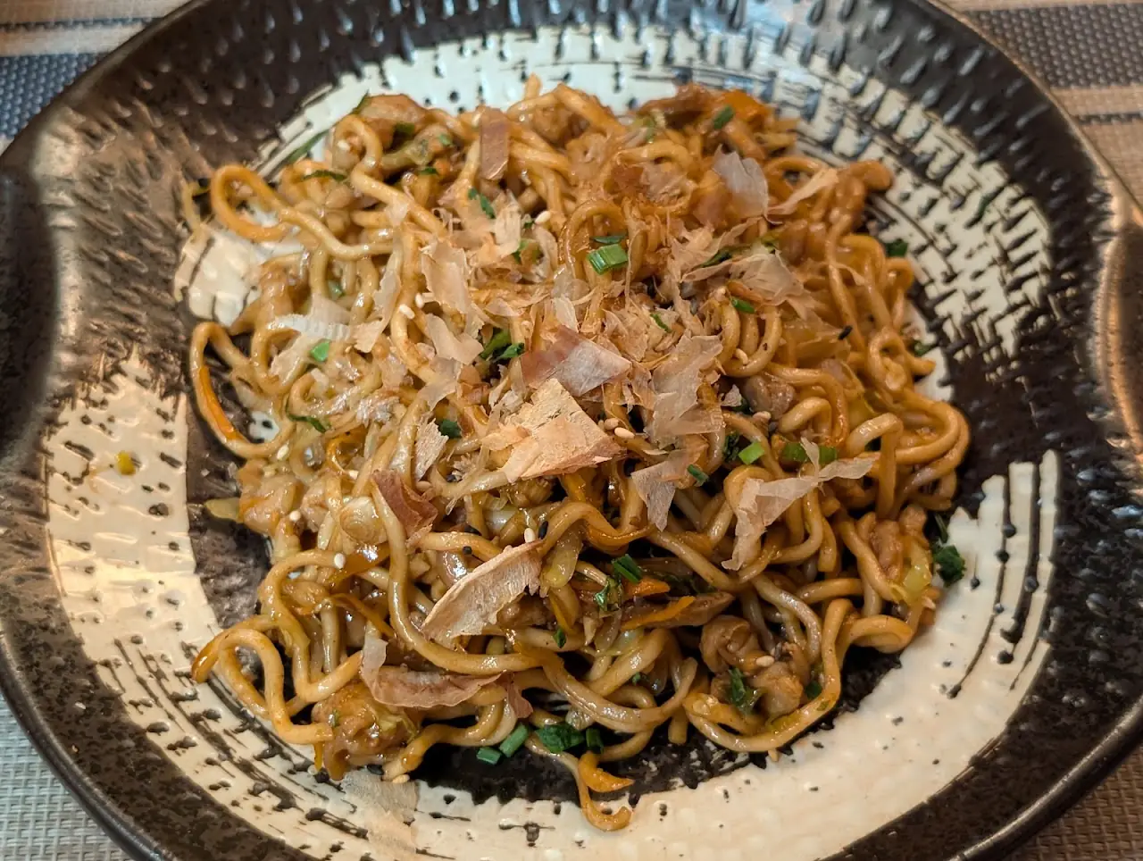 A bowl of yakisoba noodles topped with bonito flakes and scallions.