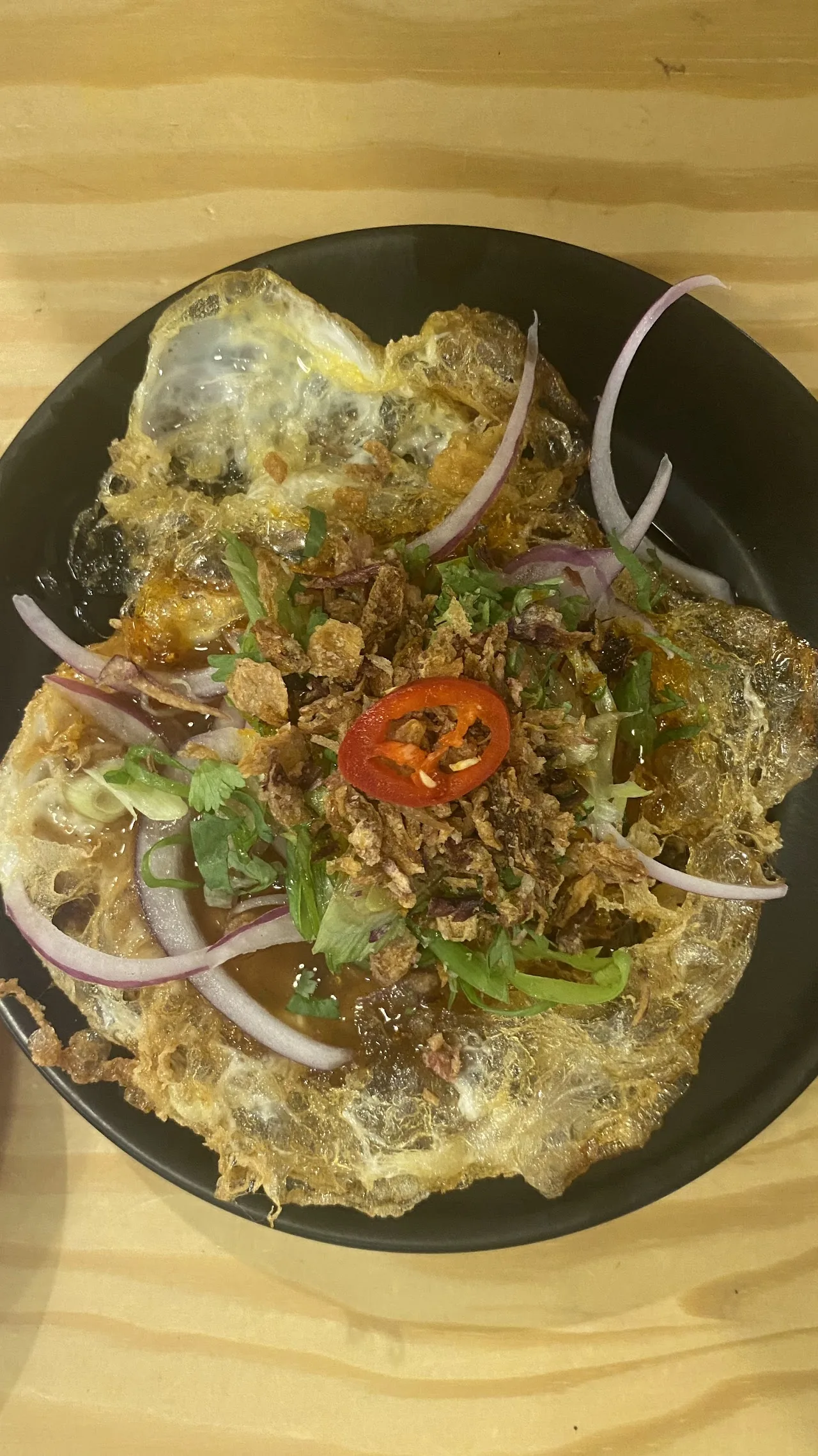 A herb salad with sliced red onion and chili on a black plate