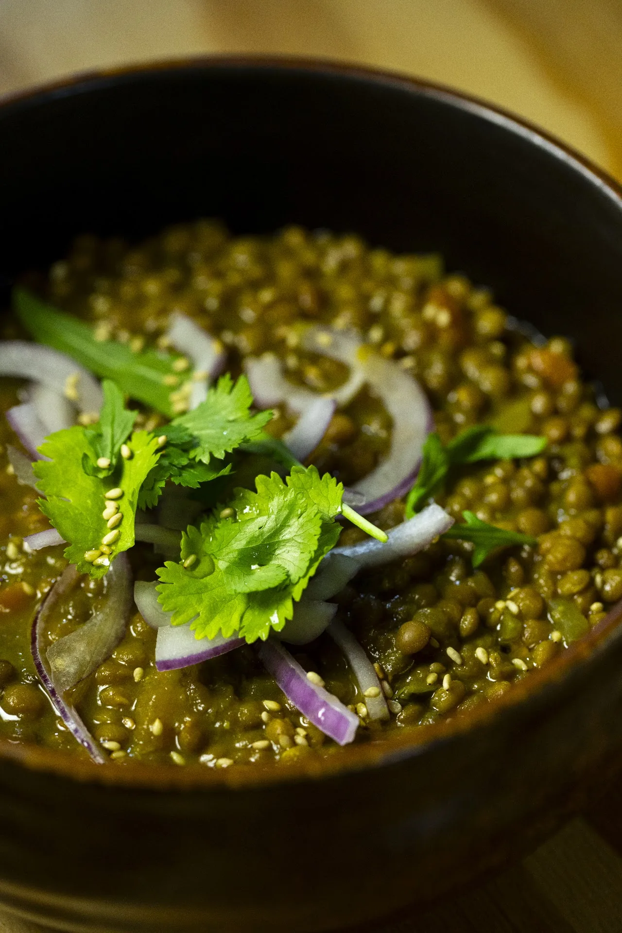 A green curry with cilantro and red onion in a dark bowl