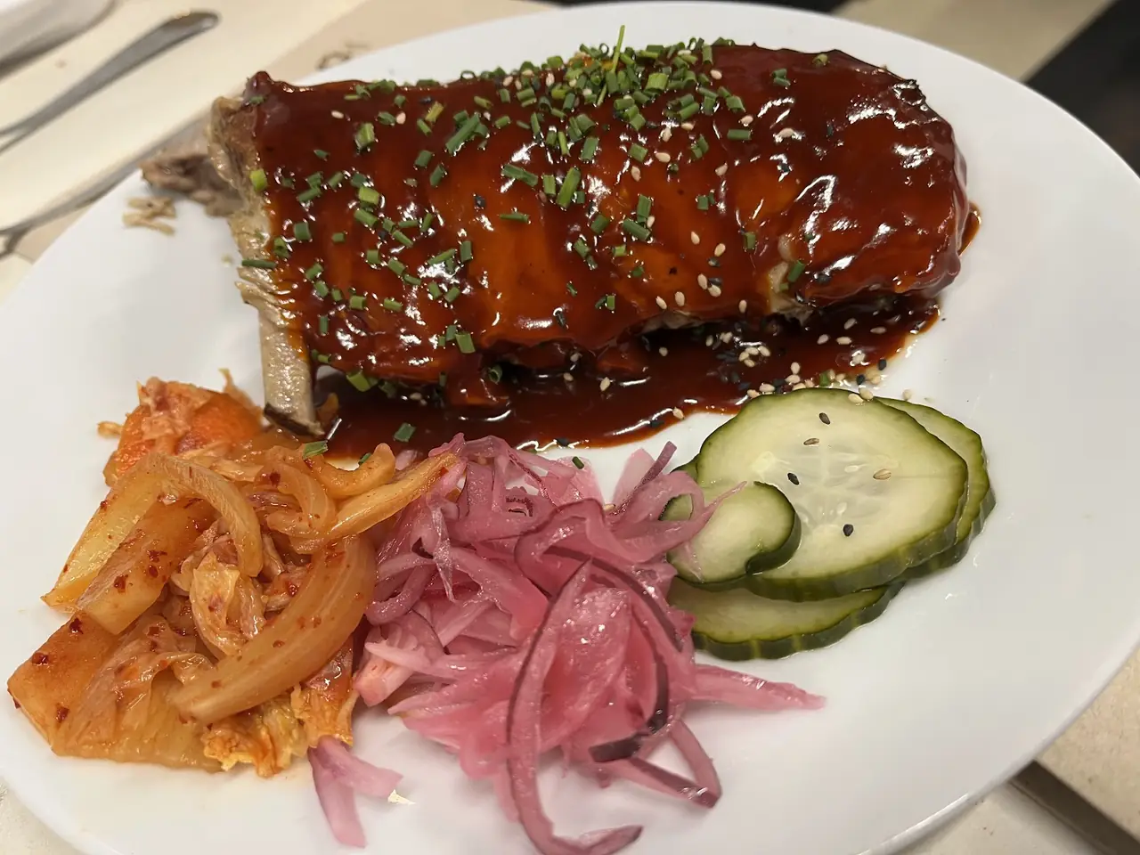 Glazed rack of ribs topped with chives and sesame, served with kimchi, pickled onion and cucumber