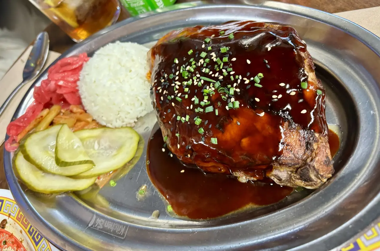 Glazed pork knuckle topped with chives and sesame, served with rice, kimchi and pickles on a metal platter