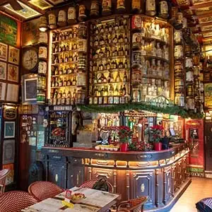 Ornate pub bar interior with shelves of liquor bottles lit from below and a curved wooden bar counter