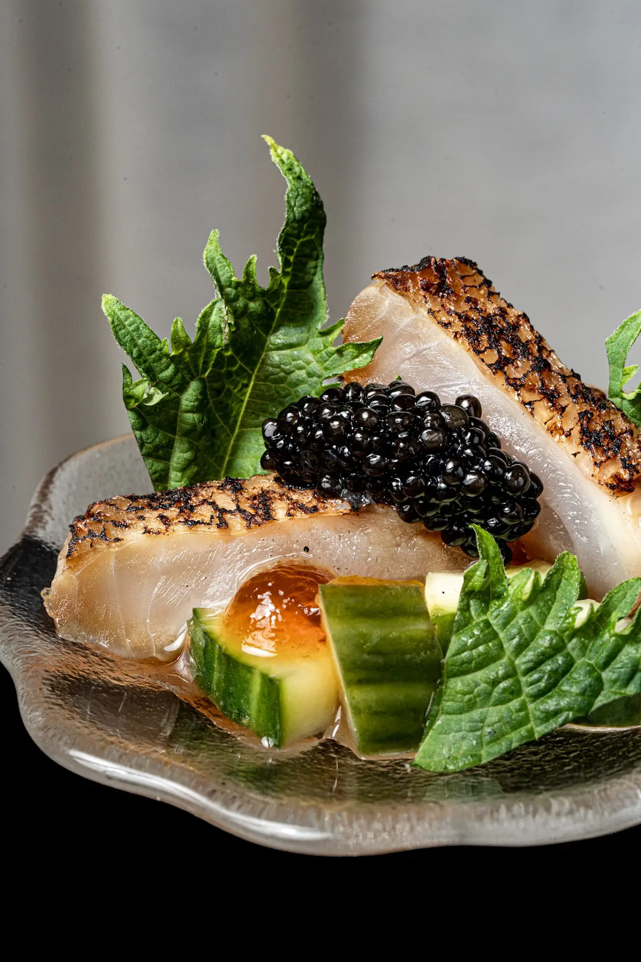 Seared fish fillet with caviar, cucumber, and shiso leaf on a ceramic plate