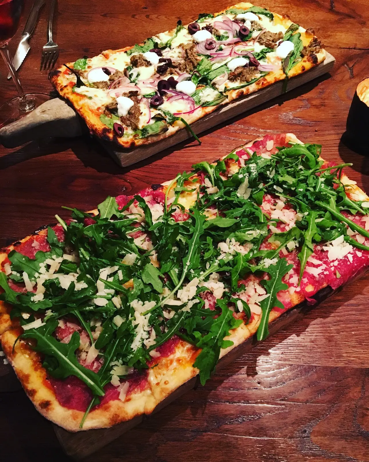 Flatbread topped with arugula, shaved cheese, and cured meat on a wooden board