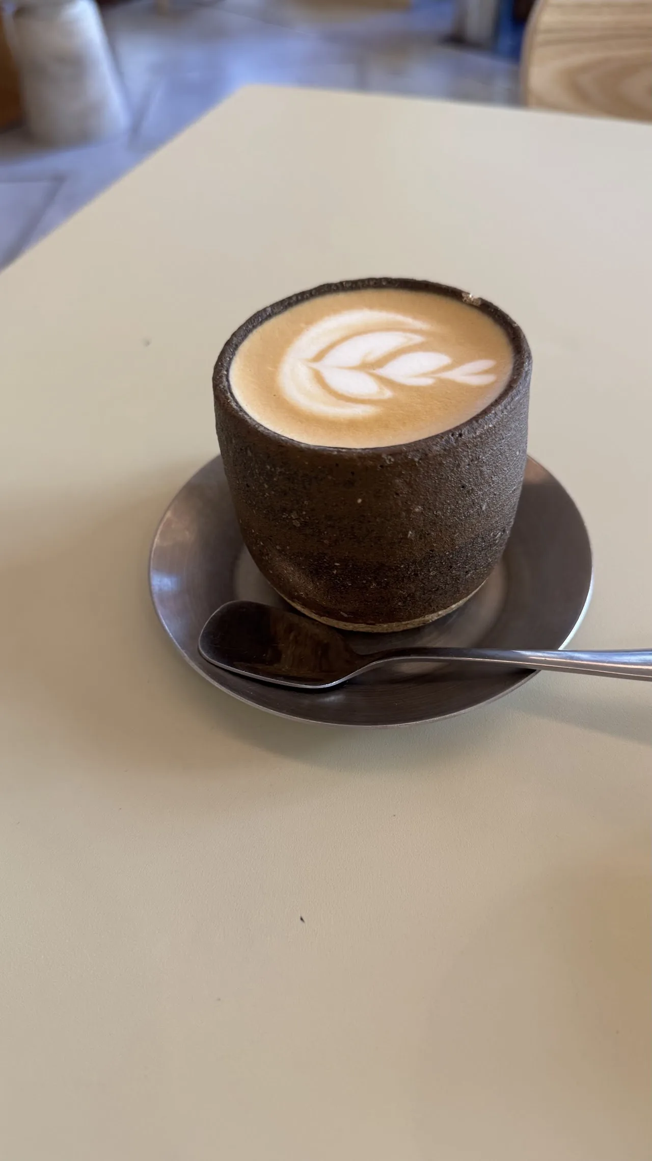 A cappuccino with leaf-pattern latte art on a white table