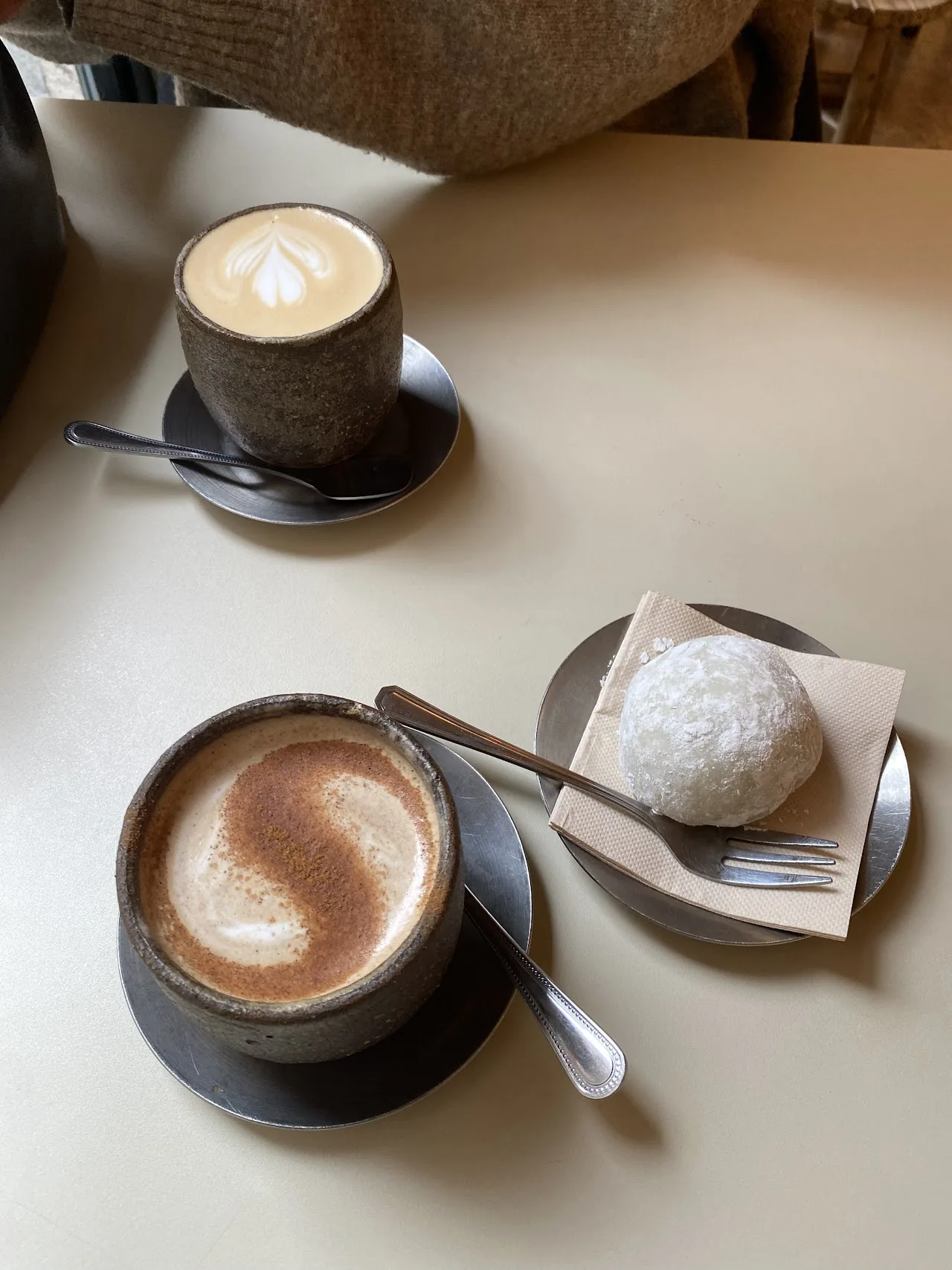 Two coffees with latte art beside a small round pastry on a plate