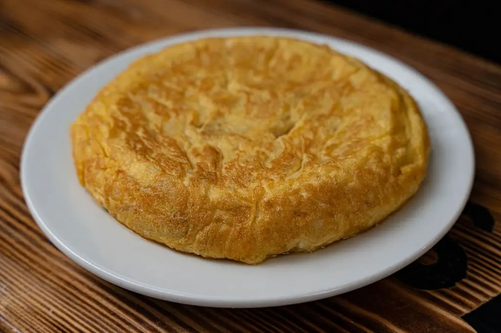 Spanish tortilla (tortilla de patatas) on a white plate on a wooden table at Koska Taverna