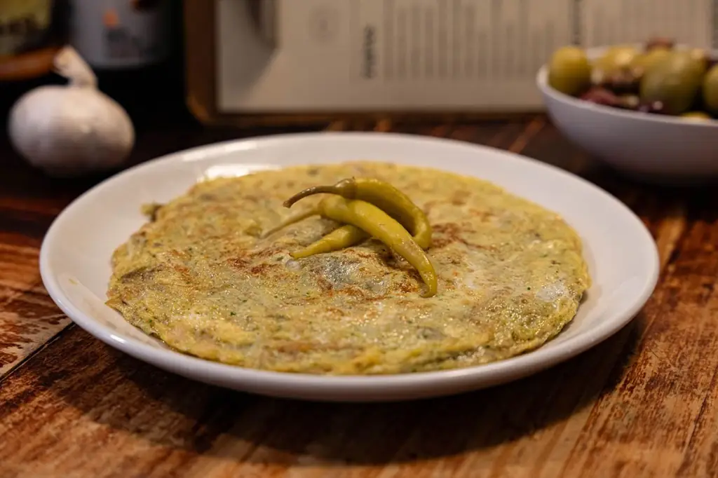 Herb omelette topped with two pickled green guindilla peppers, on a white plate at Koska Taverna