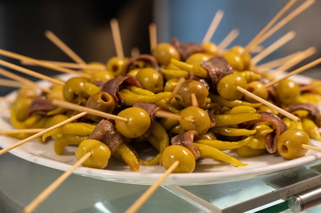 Gilda-style skewers of green olives, pickled guindilla peppers, and anchovies on a white plate at Koska Taverna