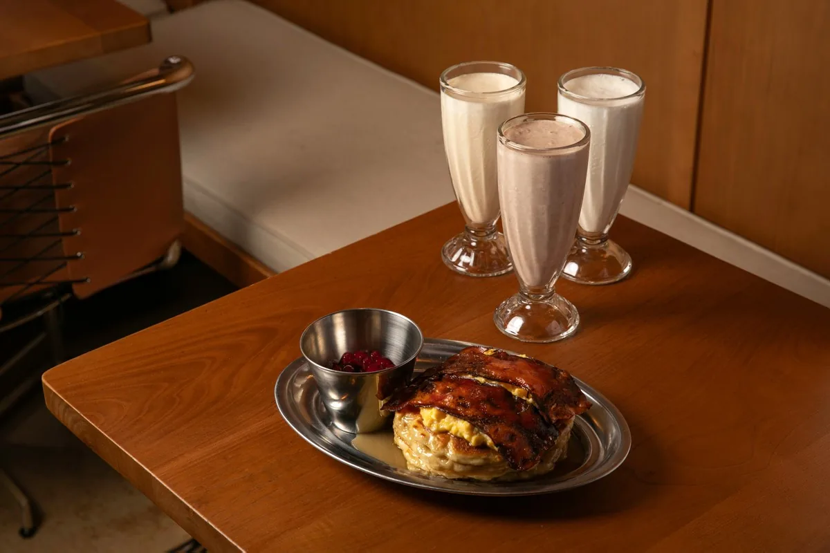 A burger platter beside three milkshakes in glasses