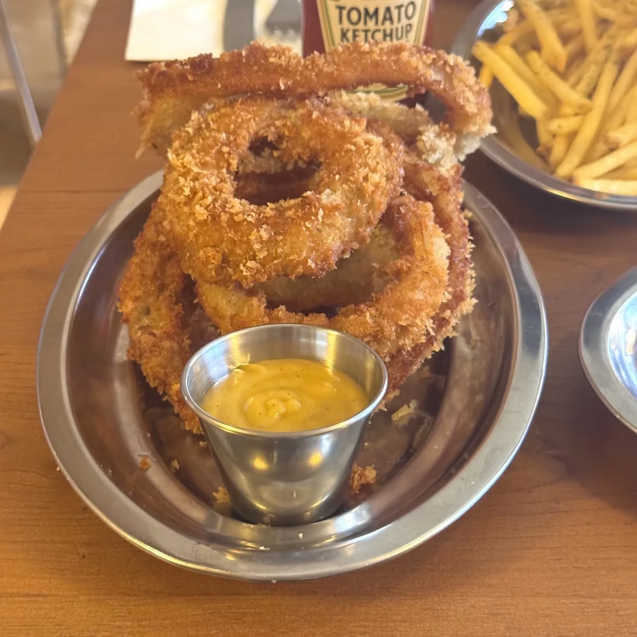 A stack of golden onion rings with a cup of dipping sauce