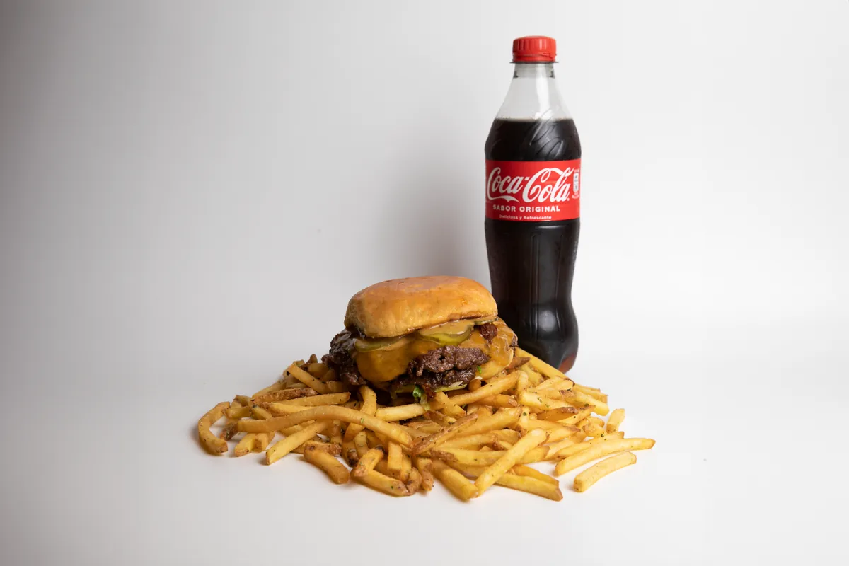 A burger and fries plated with a bottle of cola on a white background