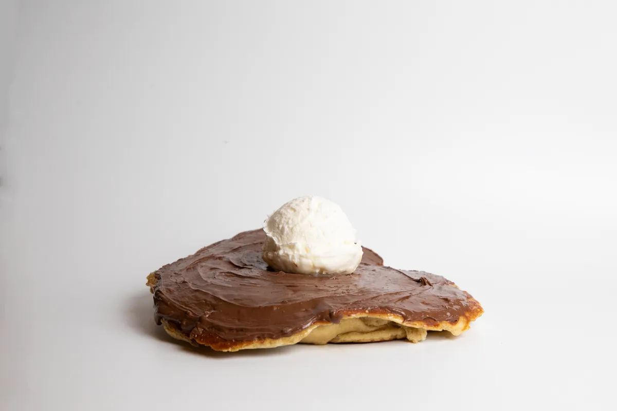 A folded chocolate crepe topped with a scoop of vanilla ice cream