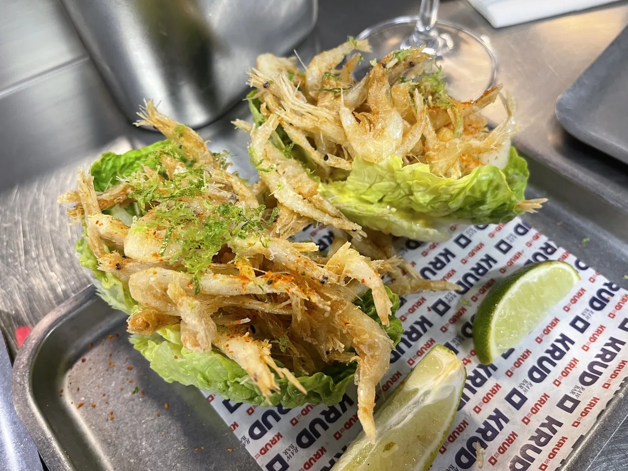 Golden fried seafood served over lettuce leaves on a metal tray with a lime wedge