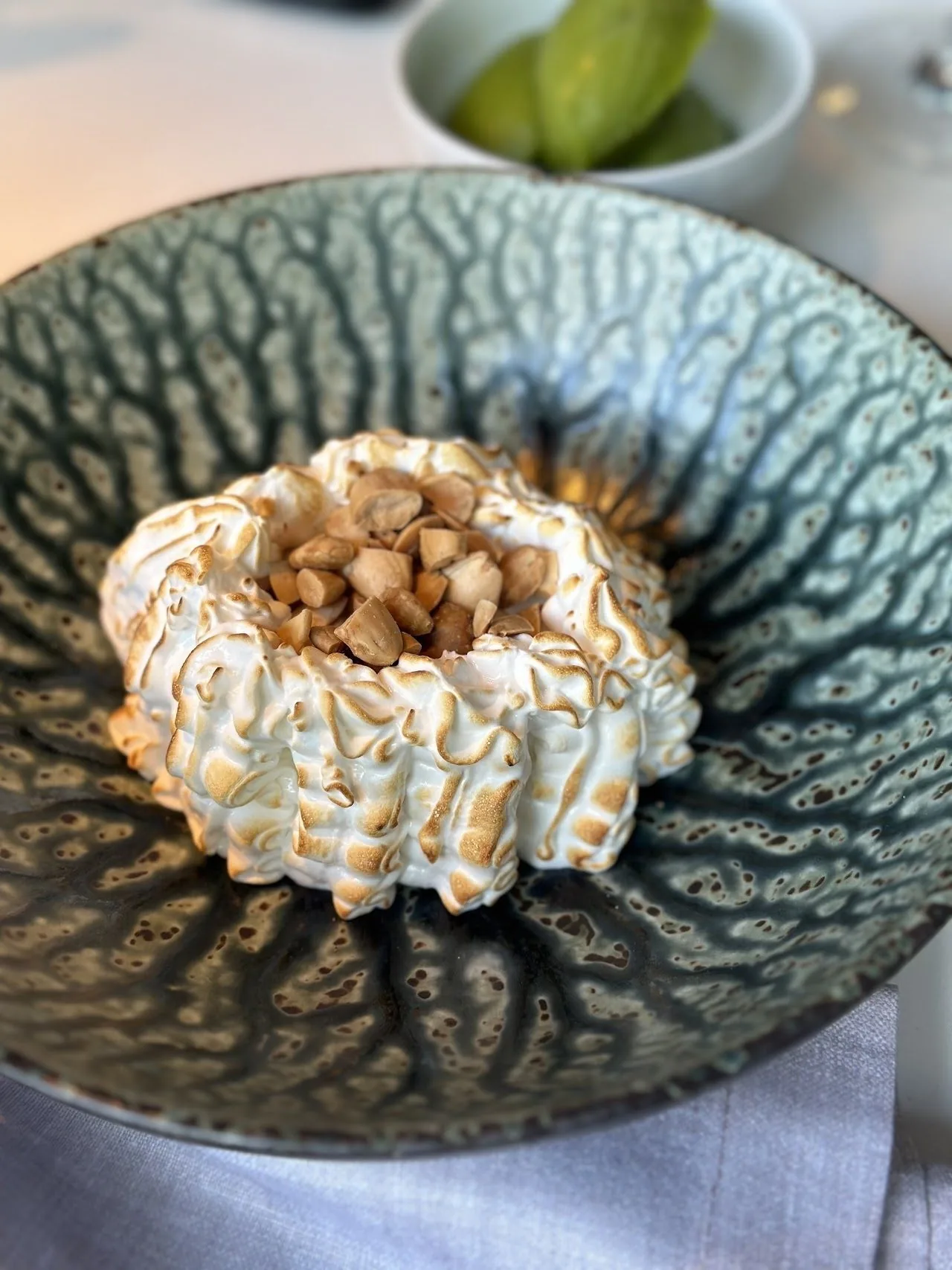 A dark patterned bowl holding a round dessert topped with meringue and nuts