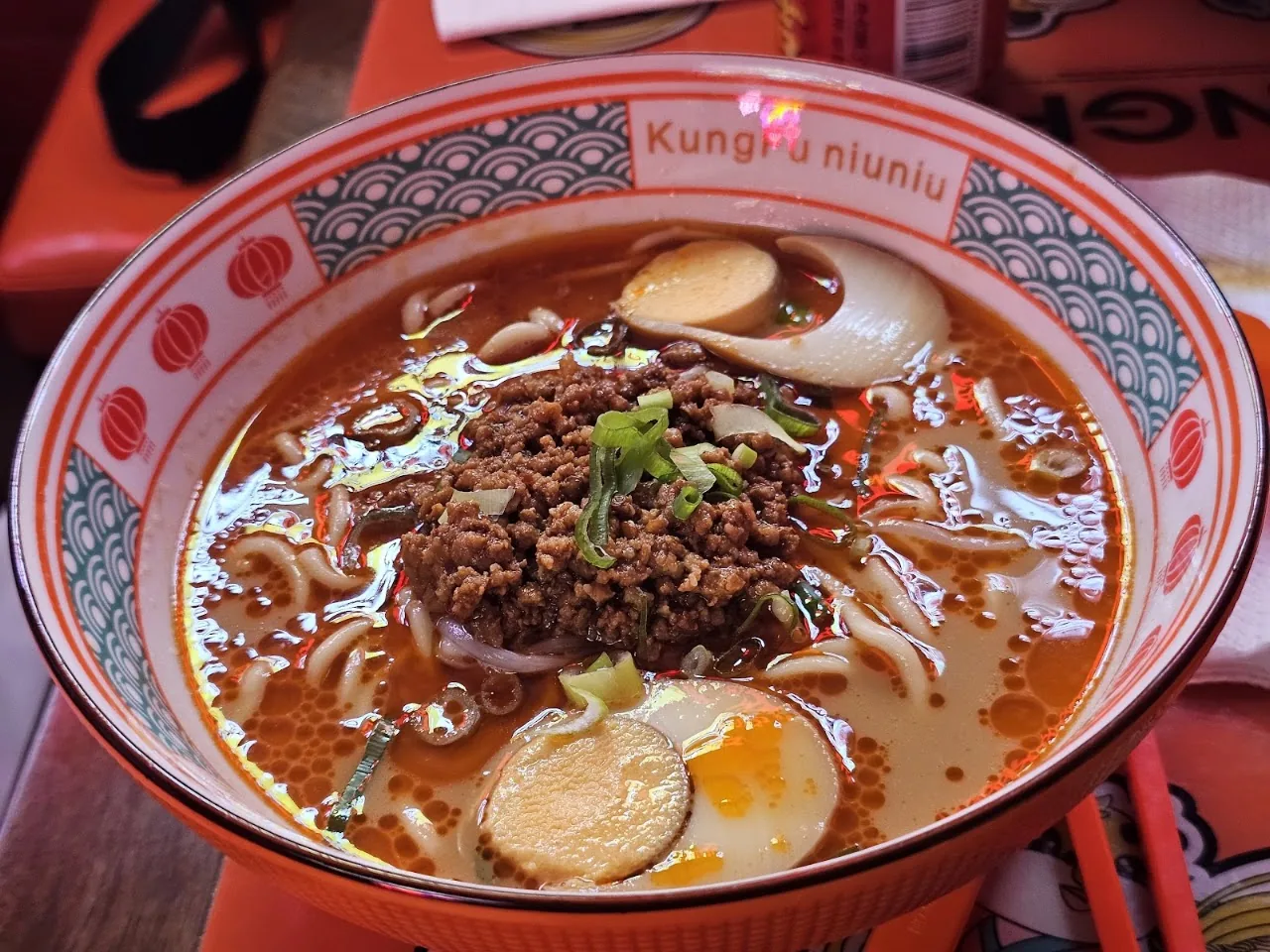 A bowl of spicy noodle soup topped with minced meat, boiled eggs, and scallions