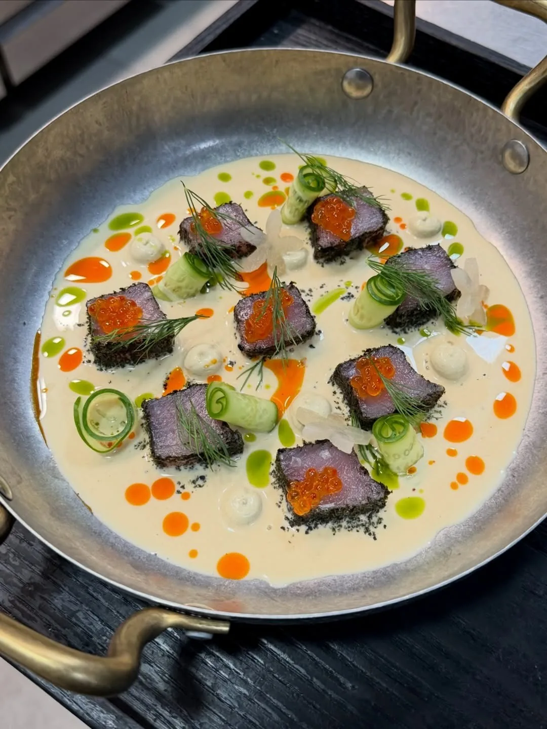A metal pan of pale broth with slices of dark fish and orange dots