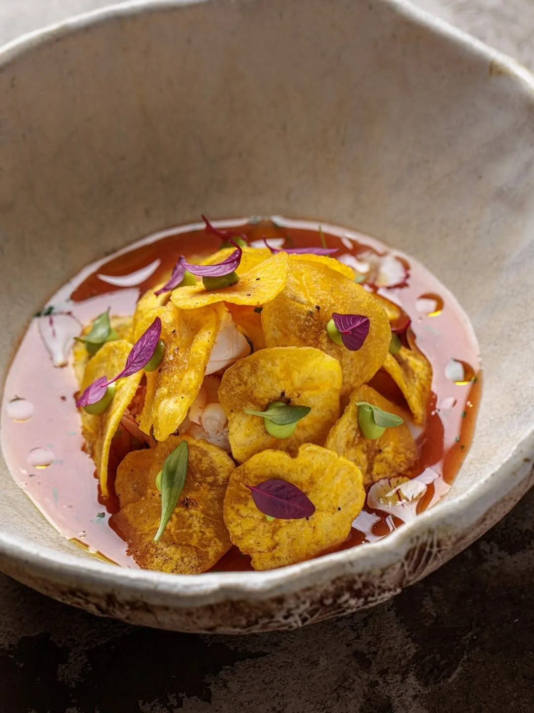 A round bowl with fried yellow slices, herbs and a pink sauce