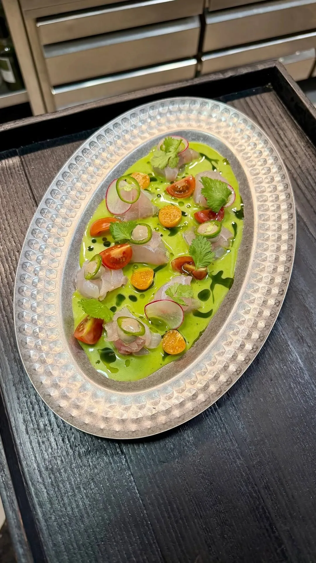 A long oval plate of raw fish and vegetables in a green sauce