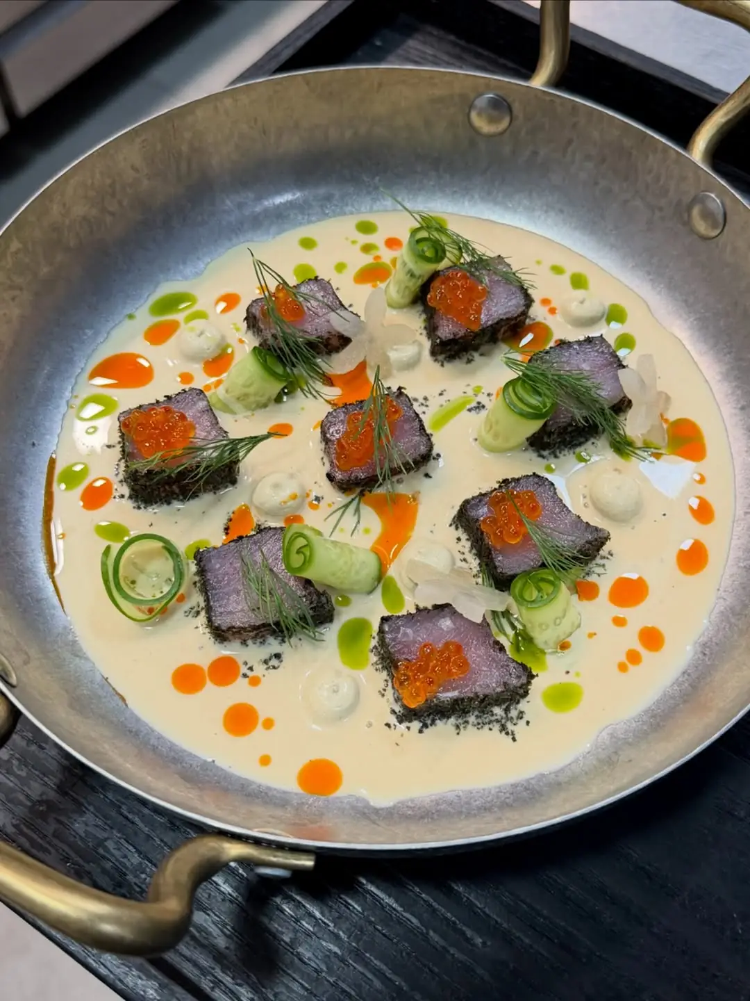 Seared tuna cubes topped with orange roe in a creamy sauce in a metal pan