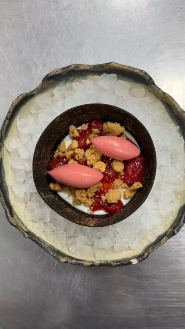 Coconut shell dessert with pink sorbet and berries set on crushed ice