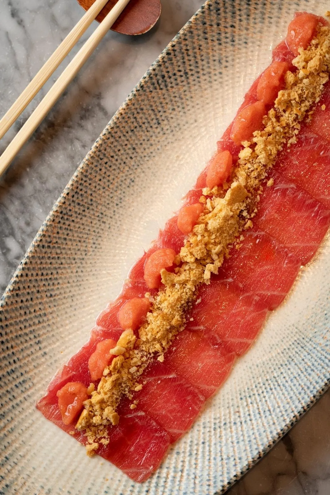 A long plate of raw fish slices topped with a crumbly golden topping