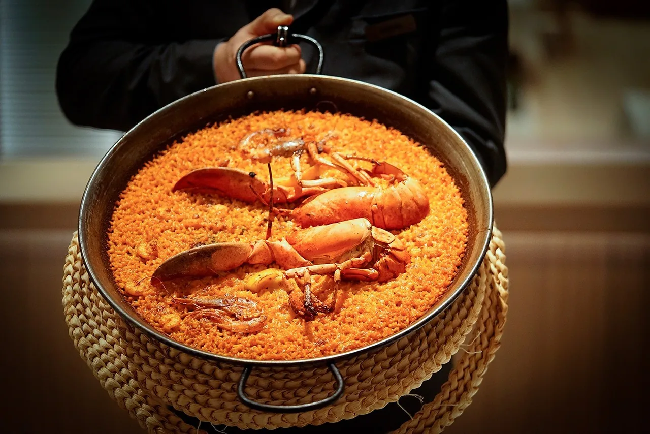 An orange rice dish with lobster in a paella pan on a woven mat