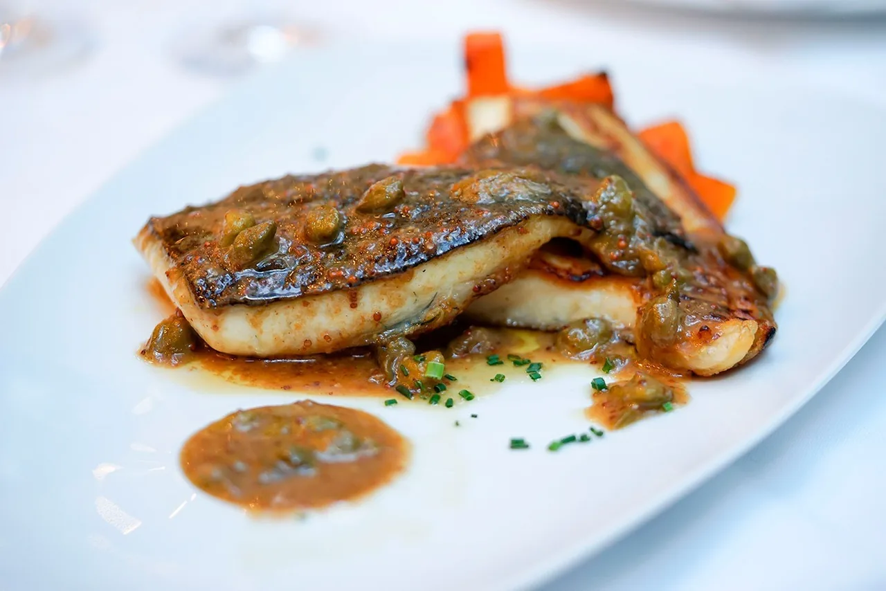 A seared fish fillet with sauce on a white plate
