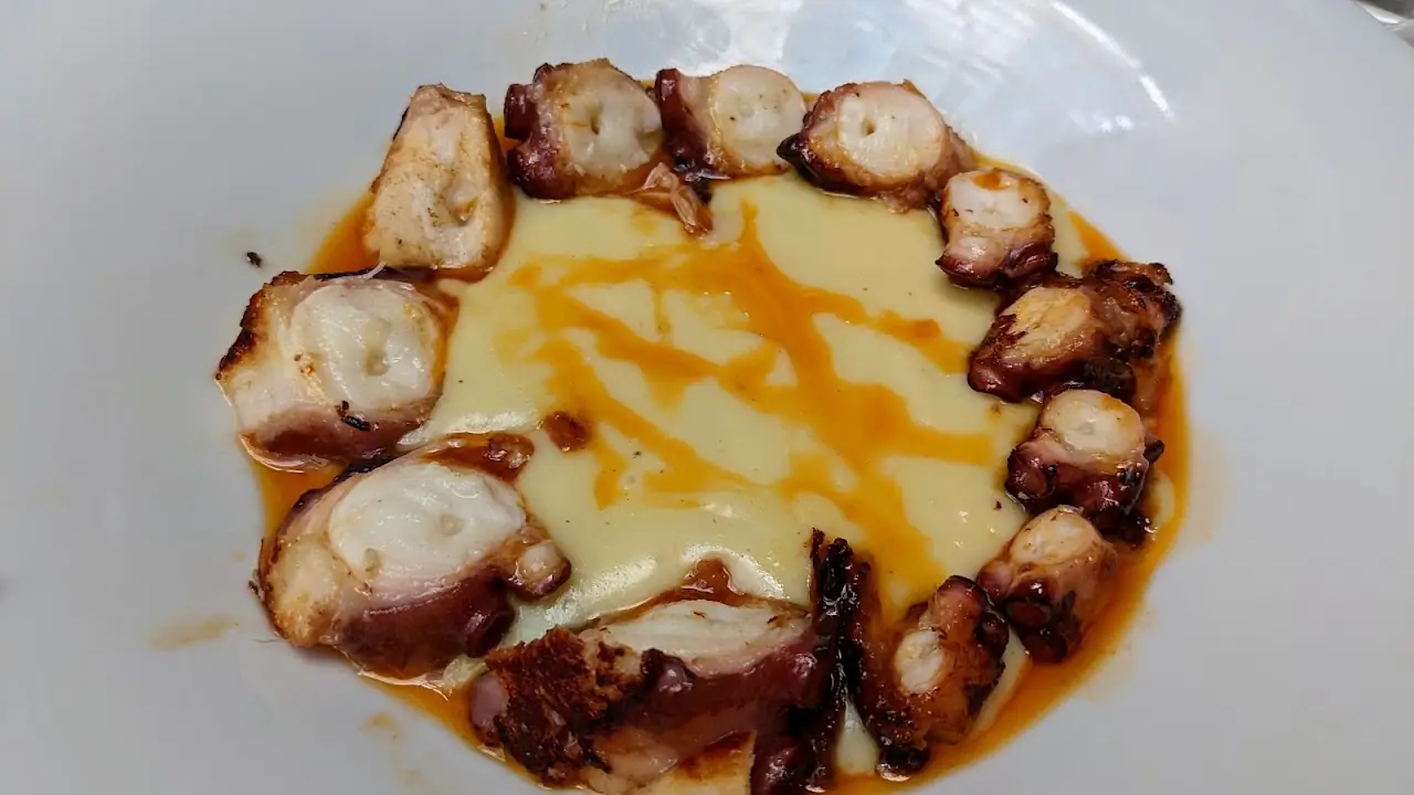 Grilled octopus arranged in a circle over an orange sauce.