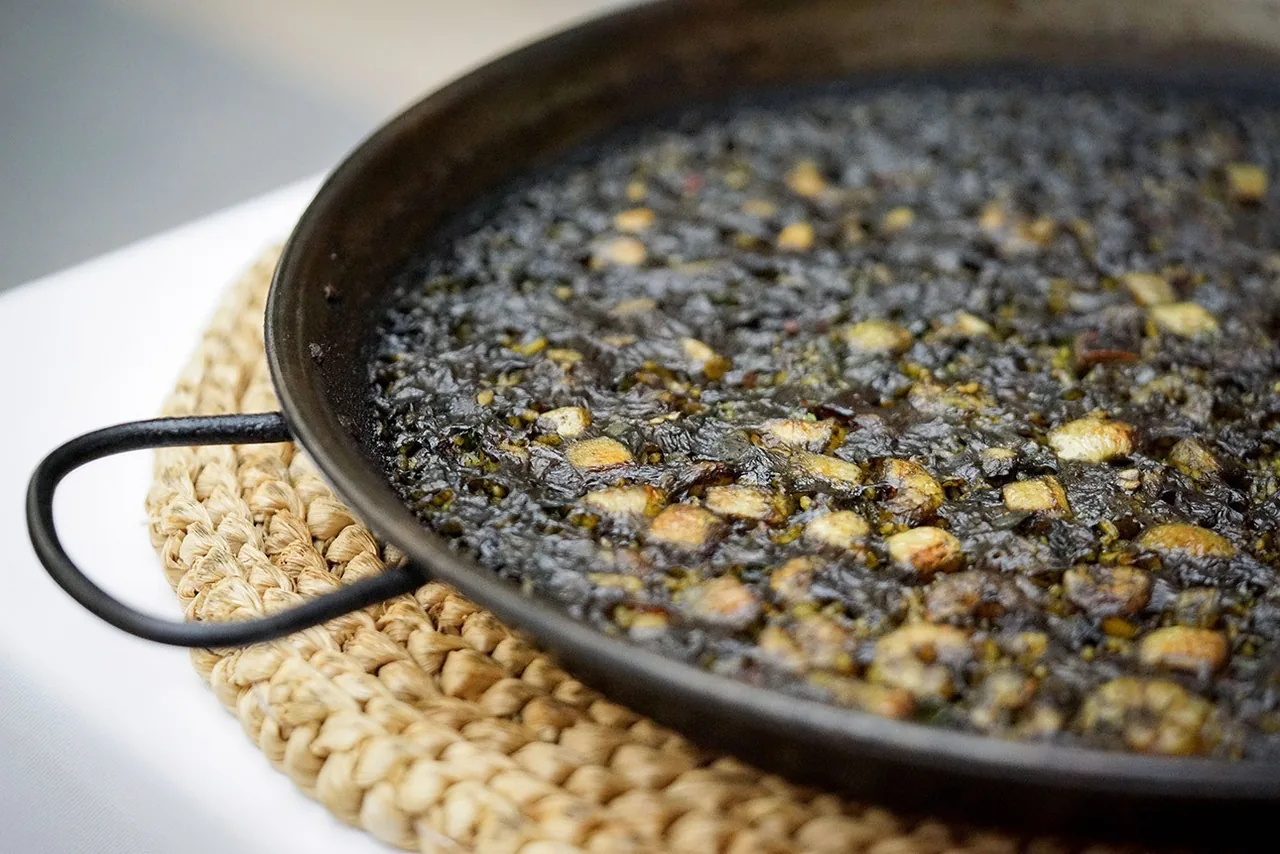 Black rice in a paella pan on a woven mat