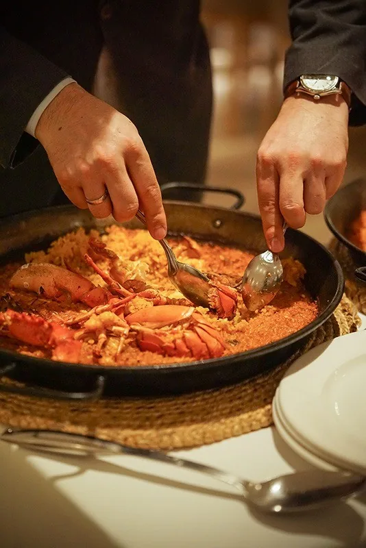 A cook serving lobster rice from the paella pan