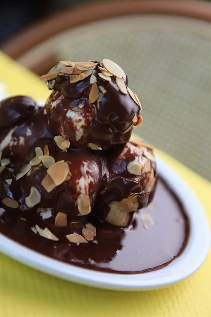 Chocolate profiteroles topped with toasted almond flakes and chocolate sauce on a white plate, at L'Entrecote
