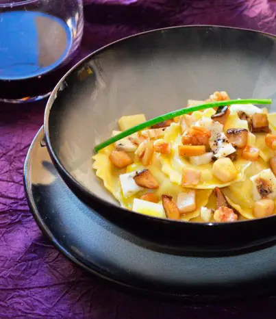 Filled pasta with wild mushrooms, diced cheese, and truffle in a dark bowl, garnished with a chive, at L'Italiano Perso