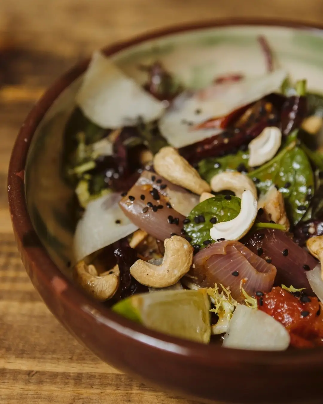 Close-up of a bowl of marinated red onion, greens, cashews, shaved cheese, and tomato sauce dressed with black sesame at La Alcoba Azul