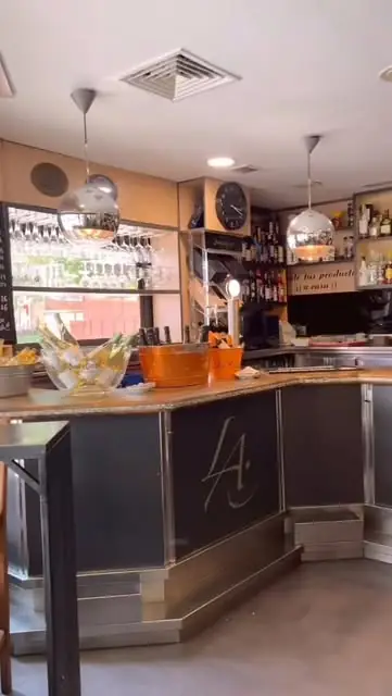 Interior of the bar with a curved black counter bearing the 'LA' monogram, pendant lights, wine glasses hung above and bottles racked behind