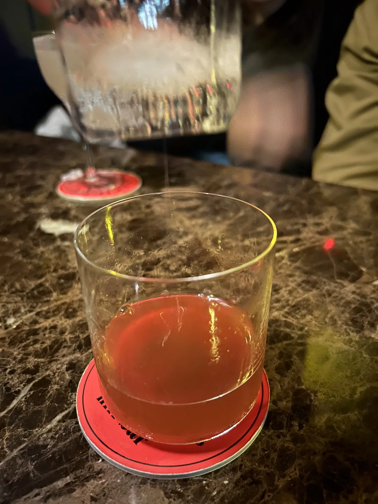 A rocks glass of an amber-red cocktail on a stone bar top